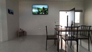 Un'area pranzo con TV a parete, un piccolo tavolo con una sedia e un tavolo da pranzo con sedie.