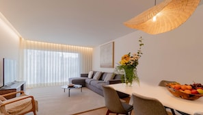 A modern living room with a sofa, coffee table, and dining table. - Home Azores - Coliseu Residences (Ponta Delgada)