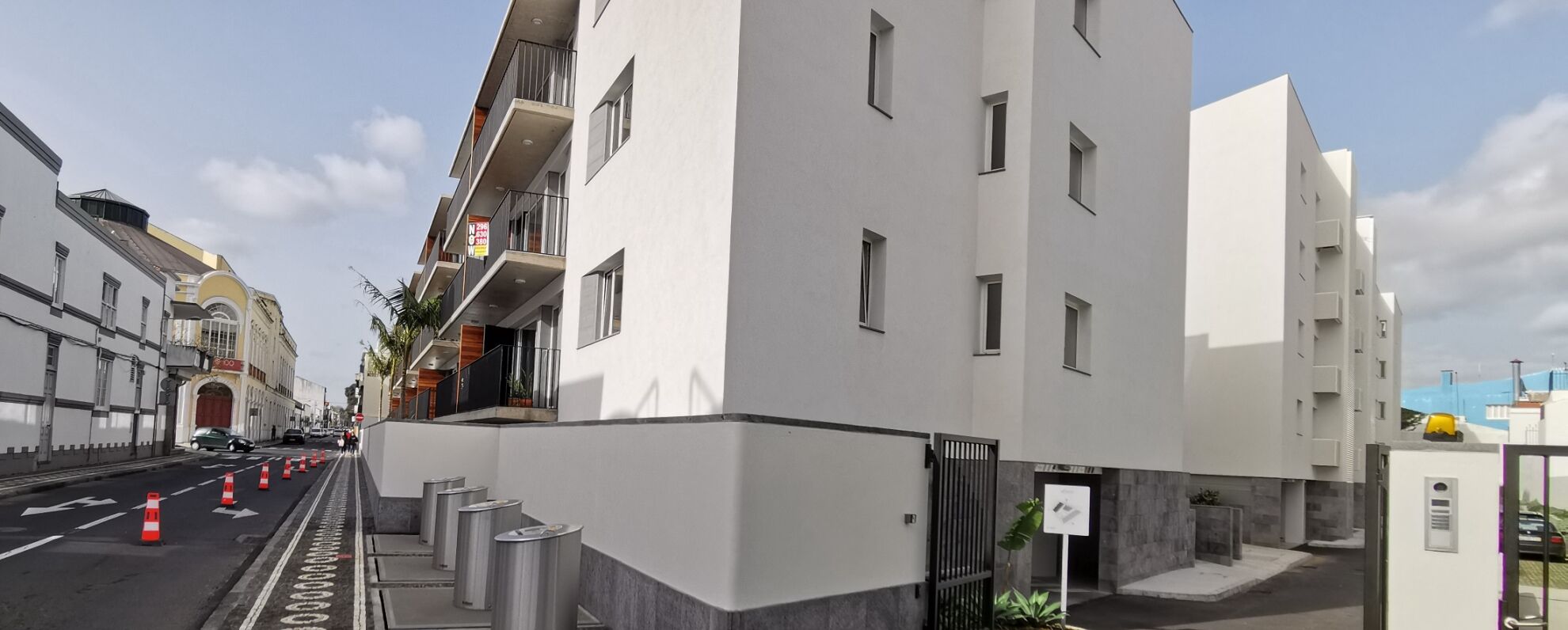 A modern building with a white facade, multiple balconies, and a gated entrance.