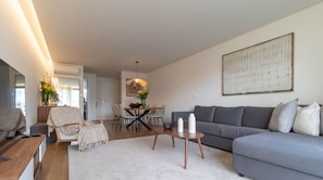 A modern living room with a grey sofa, a coffee table, and a dining area with a table and chairs. - Home Azores - Coliseu Residences (Ponta Delgada)