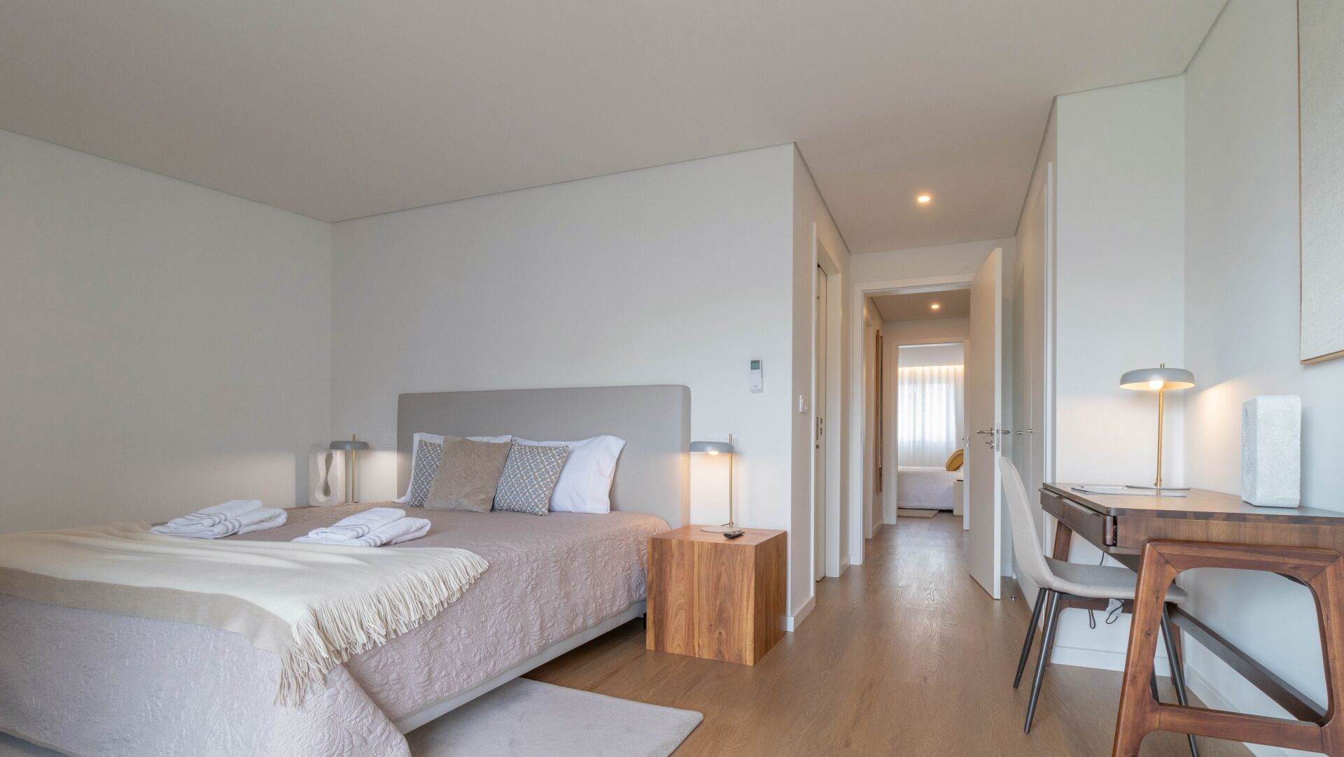A modern bedroom with a large bed, bedside tables, a desk, and a chair.