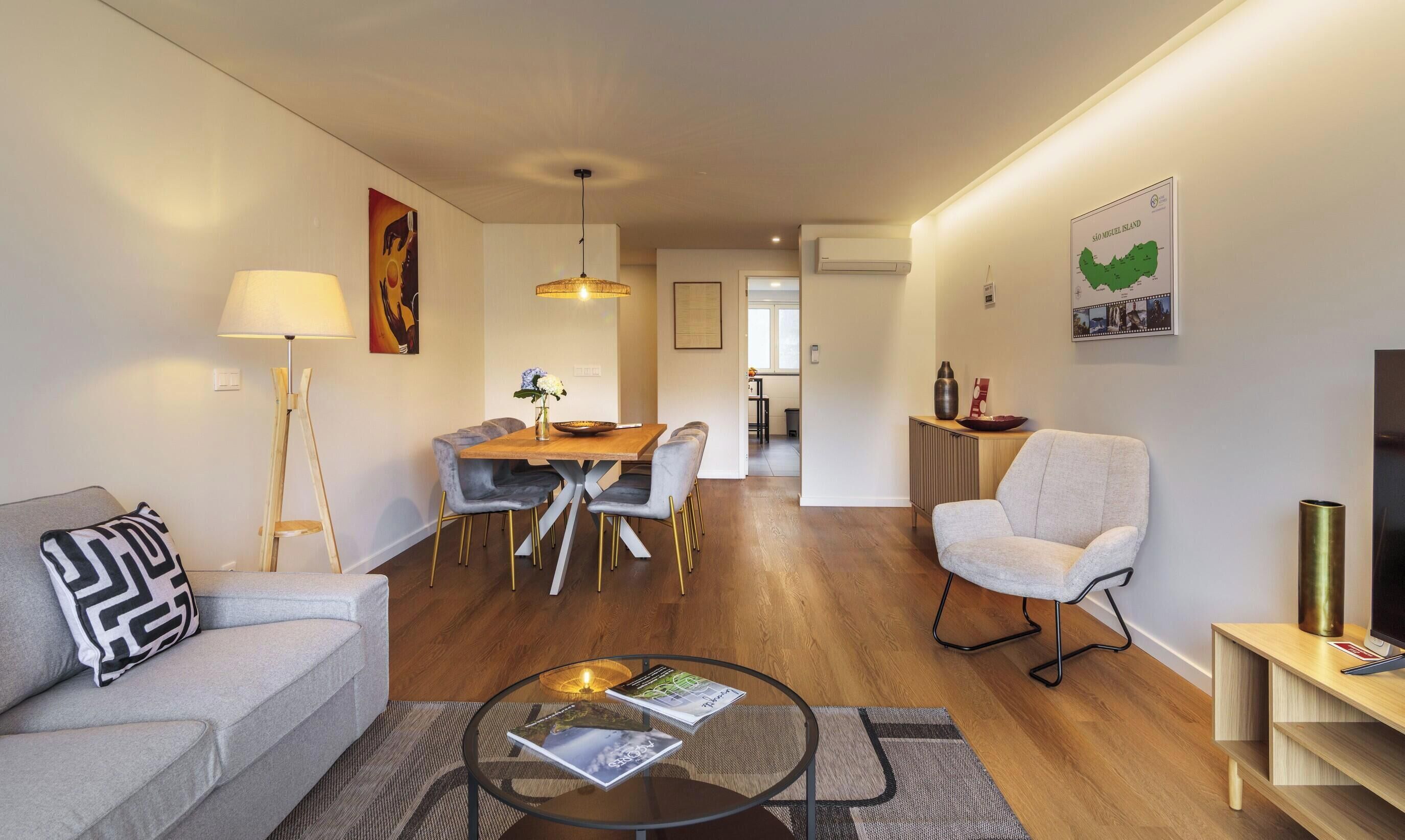 A modern living room with a sofa, a dining table with chairs, a glass coffee table, and a TV stand.