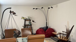 Un comedor con una mesa de vidrio, sillas marrones, un sillón de peluche rojo y una pequeña mesita de madera con un jarrón.
