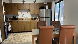 Una cocina moderna con armarios de madera, un refrigerador de acero inoxidable y un comedor con sillas de cuero marrón.