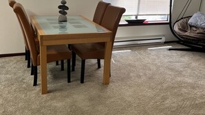 Un comedor con una mesa de vidrio, sillas marrones, una pila decorativa de piedras y una ventana con persianas.