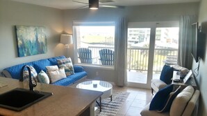 A living room with a sofa, a coffee table, a TV, and a balcony with chairs. - New Labor Day Reduction! Sunny Beach Days at Sunrise Breeze (Galveston)