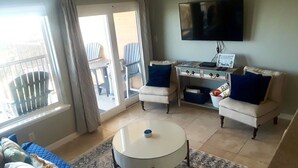 A living room with a sofa, two armchairs, a coffee table, a TV, and a balcony with chairs. - New Labor Day Reduction! Sunny Beach Days at Sunrise Breeze (Galveston)