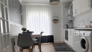 Een moderne keuken met een eethoek, een wasmachine en een groot raam met dunne gordijnen.