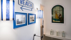 Een gang met een 'BEACH' bord, ingelijste foto’s en een glas-in-loodraam.
