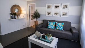 Een woonkamer met een grijze bank, een witte salontafel en een muur versierd met ingelijste foto's.