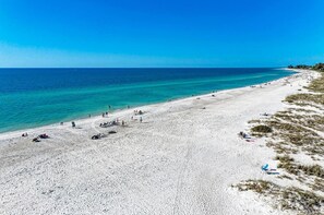 A wide sandy beach with clear turquoise water, a few people, and some beach chairs. - Liddie's Place: Gulf Front Sun Plaza West Condo, Pool, Tennis by Anna Maria Life Vacation Rentals (Holmes Beach)