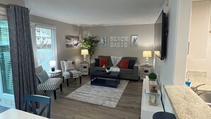 A modern living room with a sofa, coffee table, and chairs. There is a dining table with chairs. The room has a kitchen area with a countertop and sink. - Sandpiper Cove 1044 Beach Services  (Destin)