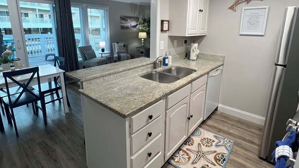 A modern kitchen with a granite countertop, white cabinets, and a stainless steel refrigerator. - Sandpiper Cove 1044 Beach Services  (Destin)