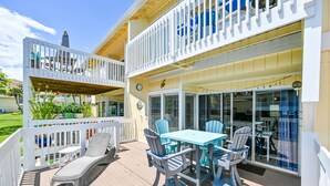 A covered outdoor deck with a table and chairs, a lounge chair, and a second-story balcony with a railing. - Sandpiper Cove 1044 Beach Services  (Destin)