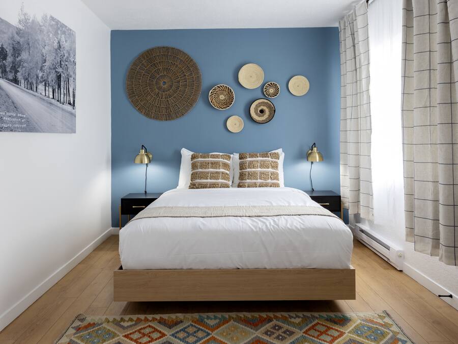 A bedroom with a bed, two bedside tables, a wall-mounted lamp, and a patterned rug.