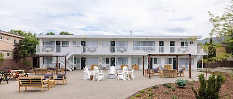 A two-story motel with a covered outdoor seating area, multiple rooms, and a landscaped garden.