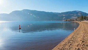 A calm lake with a sandy beach and mountains in the background. - Kettle Valley Beach Resort (Penticton)