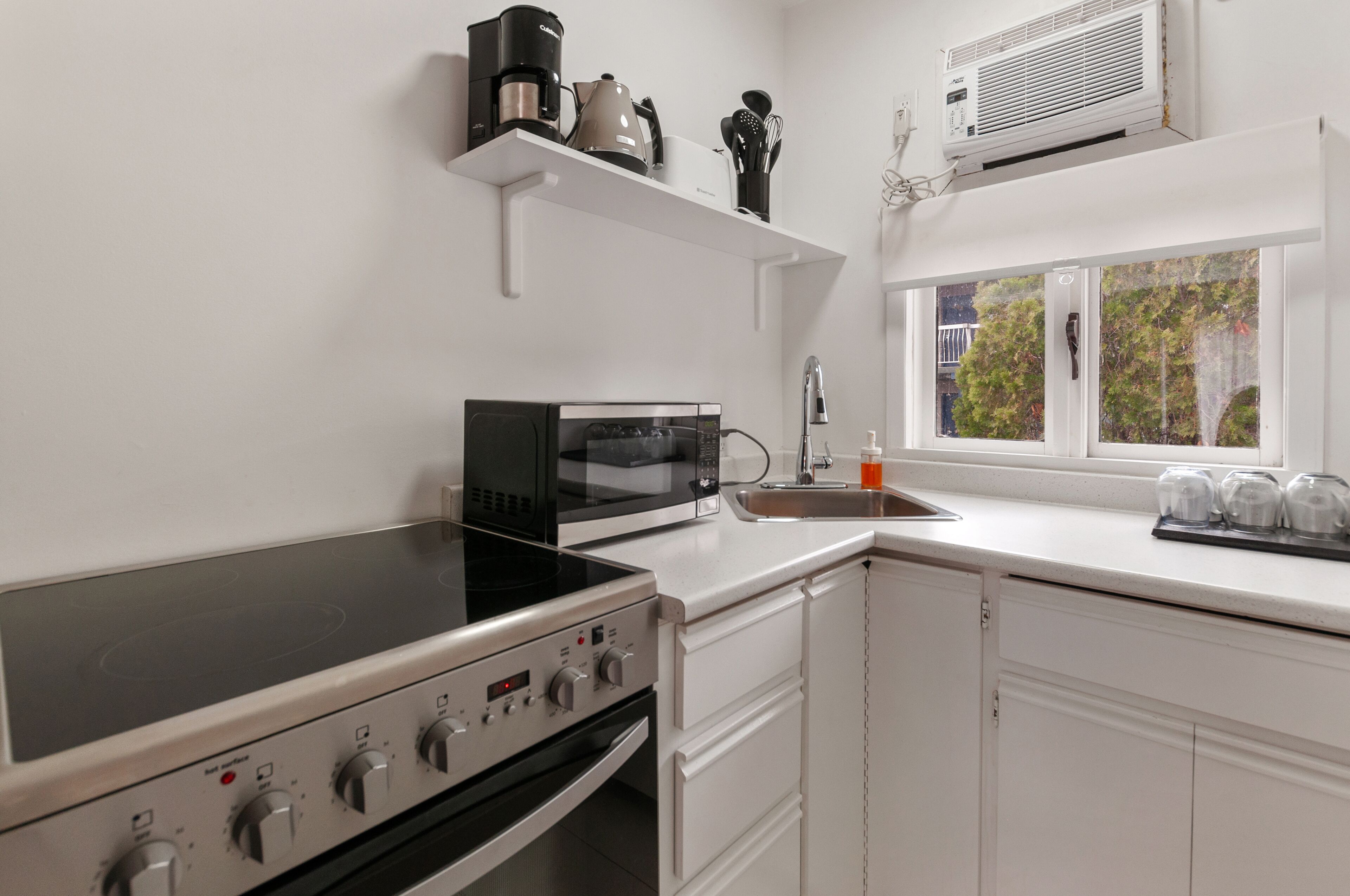 A modern kitchen with a stove, microwave, and sink. There is a window with a view of trees outside.