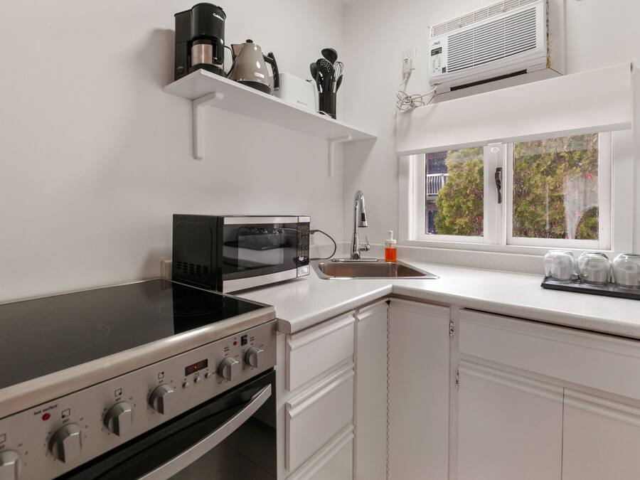 A modern kitchen with a stove, microwave, and sink. There is a window with a view of trees outside.