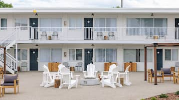 A two-story building with a balcony on the upper floor, furnished with white chairs and tables, and a fire pit in the center.