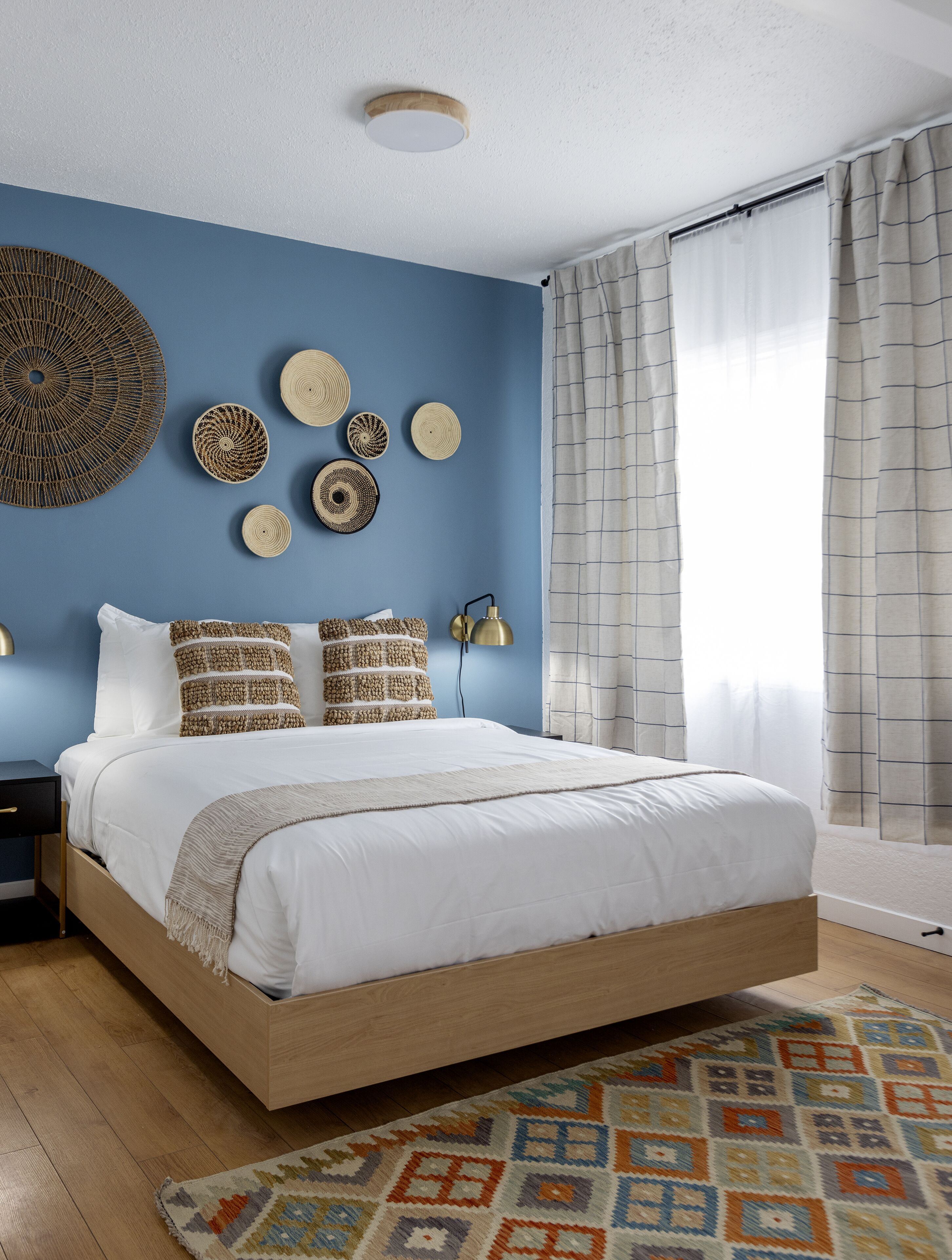 Un dormitorio con cama, lámpara de pared y alfombra estampada.