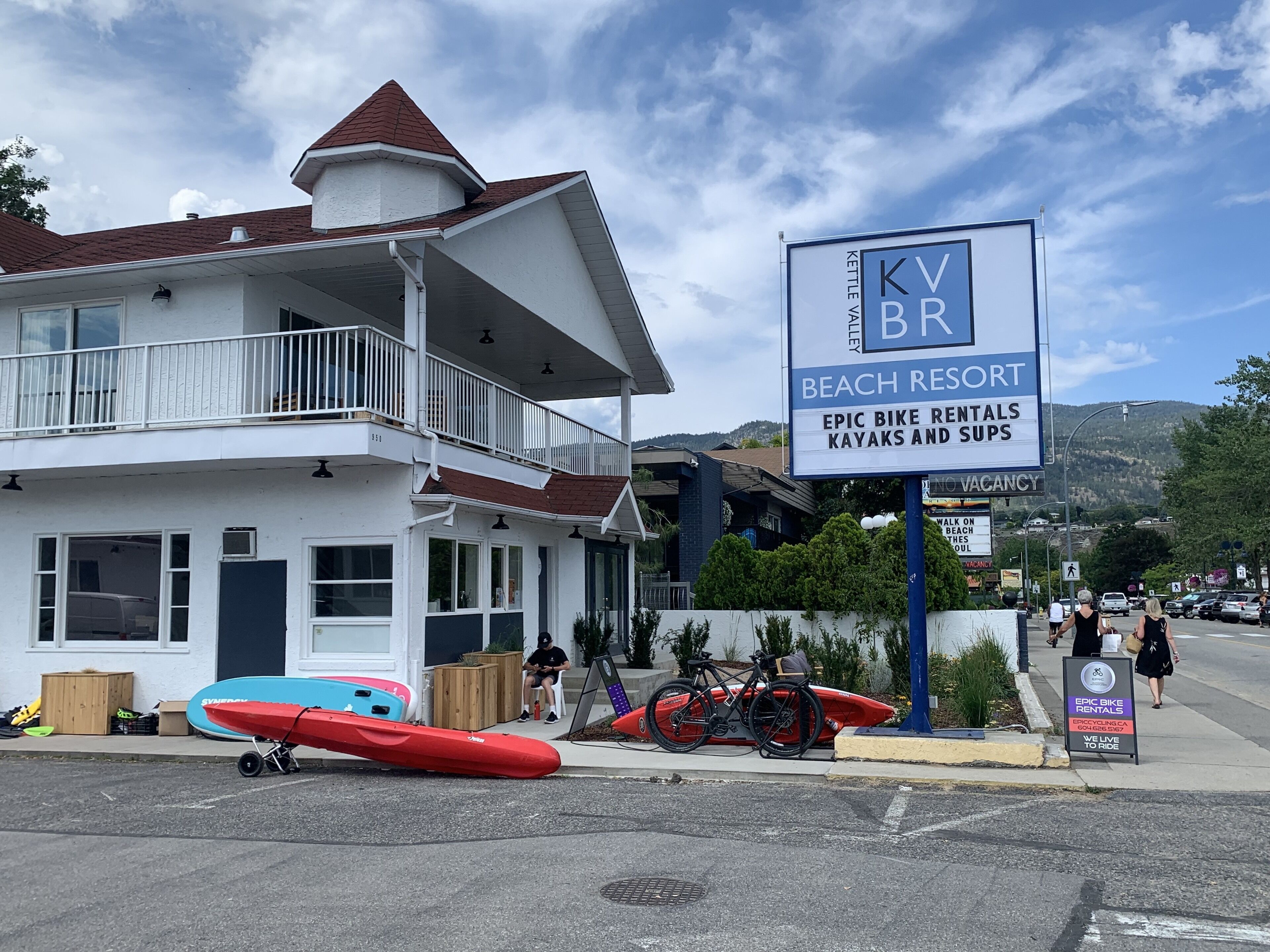 Un complejo turístico en la playa con un cartel que anuncia alquiler de kayaks y tablas de surf.