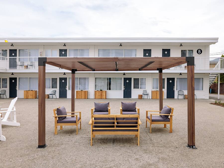 Un motel con un área de estar al aire libre cubierta, varias habitaciones y una estructura de dos pisos.