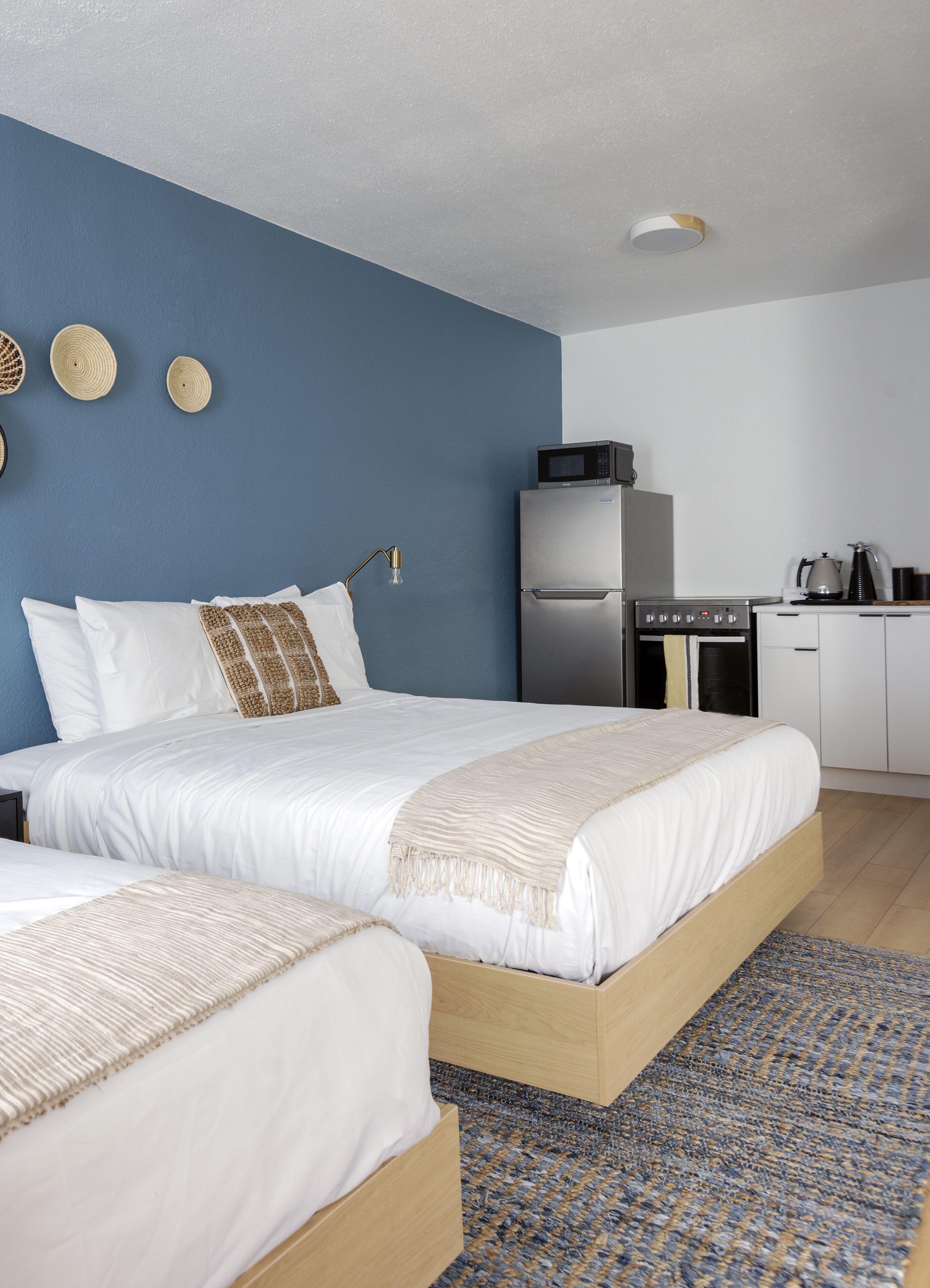 Una habitación de hotel moderna con una cama grande, una kitchenette y una pared de acento azul.