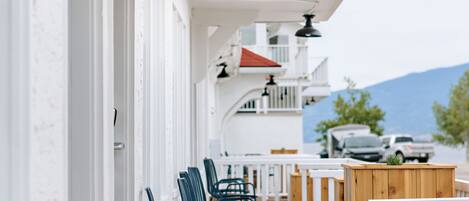 A covered outdoor seating area with rows of chairs and wooden tables, white railings, and a view of a mountain in the background.