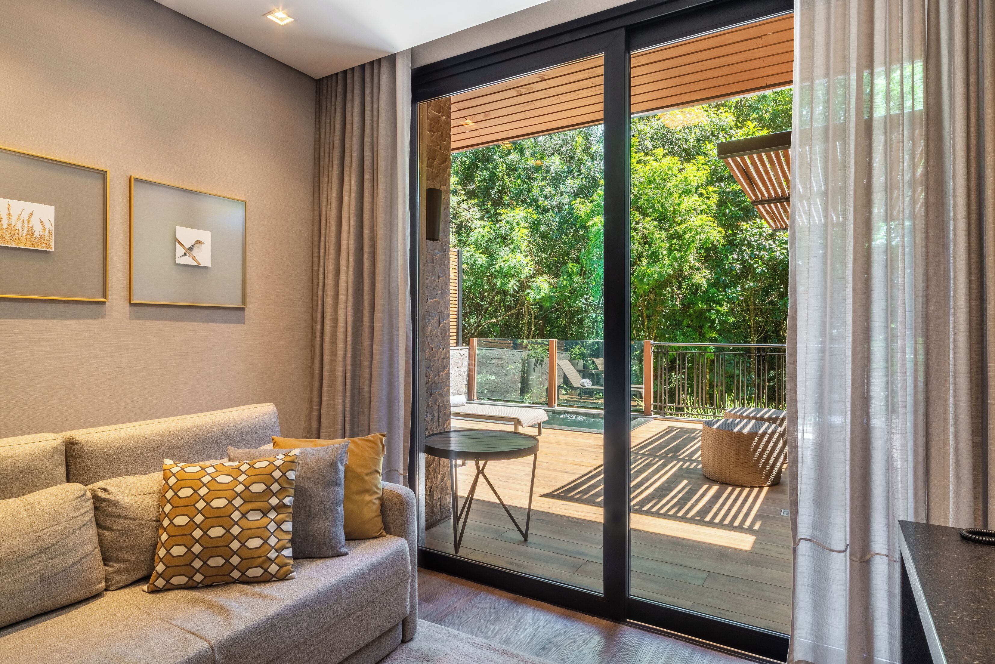 Een moderne woonkamer met een bank, kussens, een klein rond tafeltje en een schuifdeur naar een terras met uitzicht op groen.