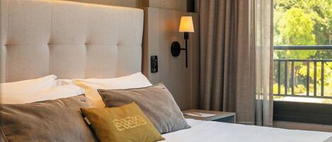 A neatly made bed with a headboard, two pillows, a bedside table with a lamp, and a view of greenery outside.