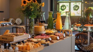 A buffet with various food items, including bread, cheeses, and meats. There are also several vases with flowers and a large wheel chair in the background. - Château Laghetto Collection (Gramado)