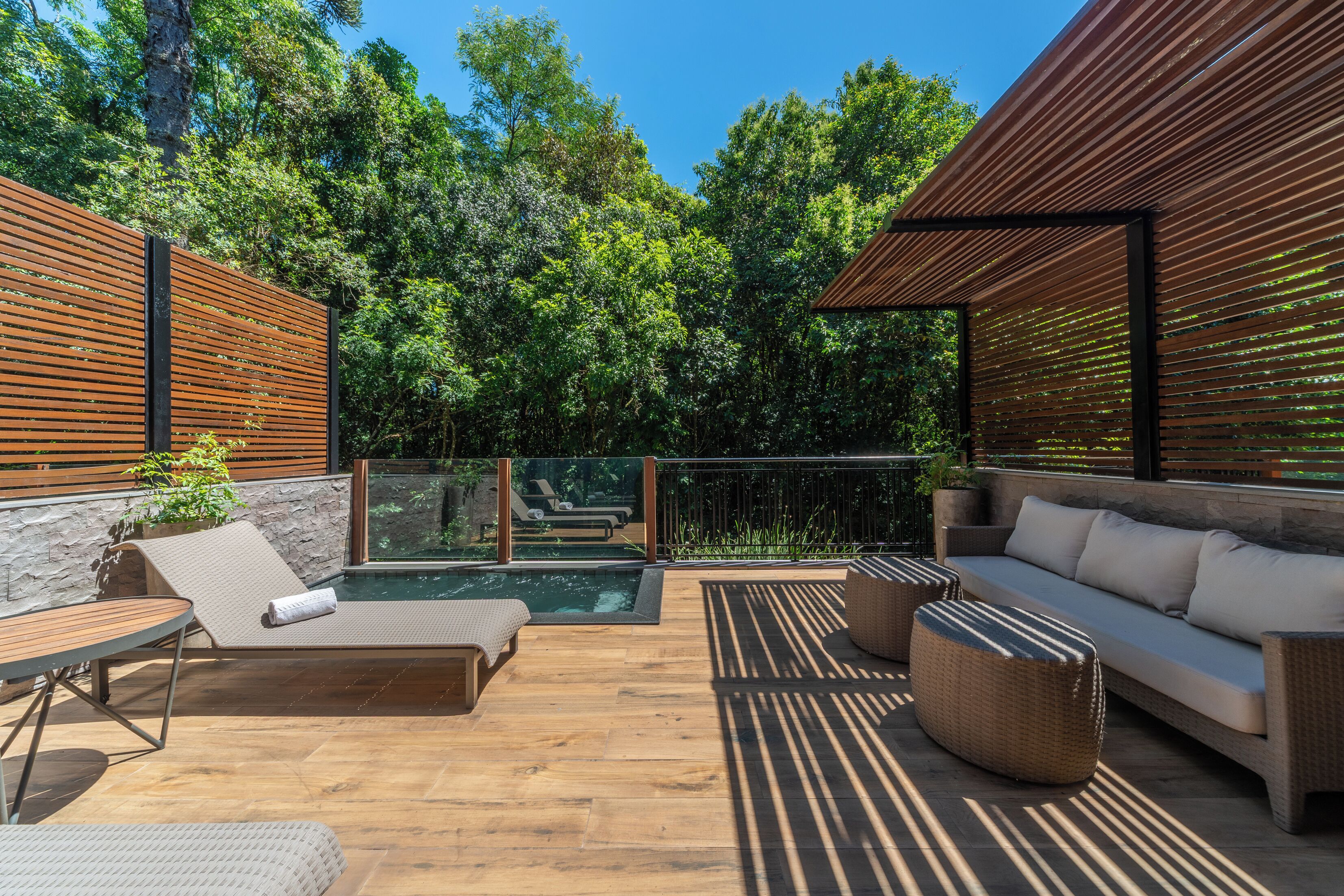 A sunlit outdoor patio with a pool, lounge chairs, and a sofa.