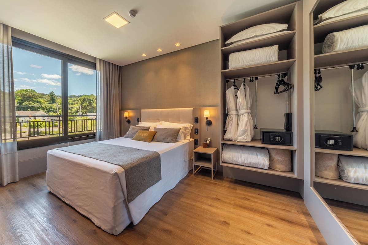 Une chambre d’hôtel moderne dotée d’un grand lit, d’un dressing et offrant une vue sur l’extérieur.