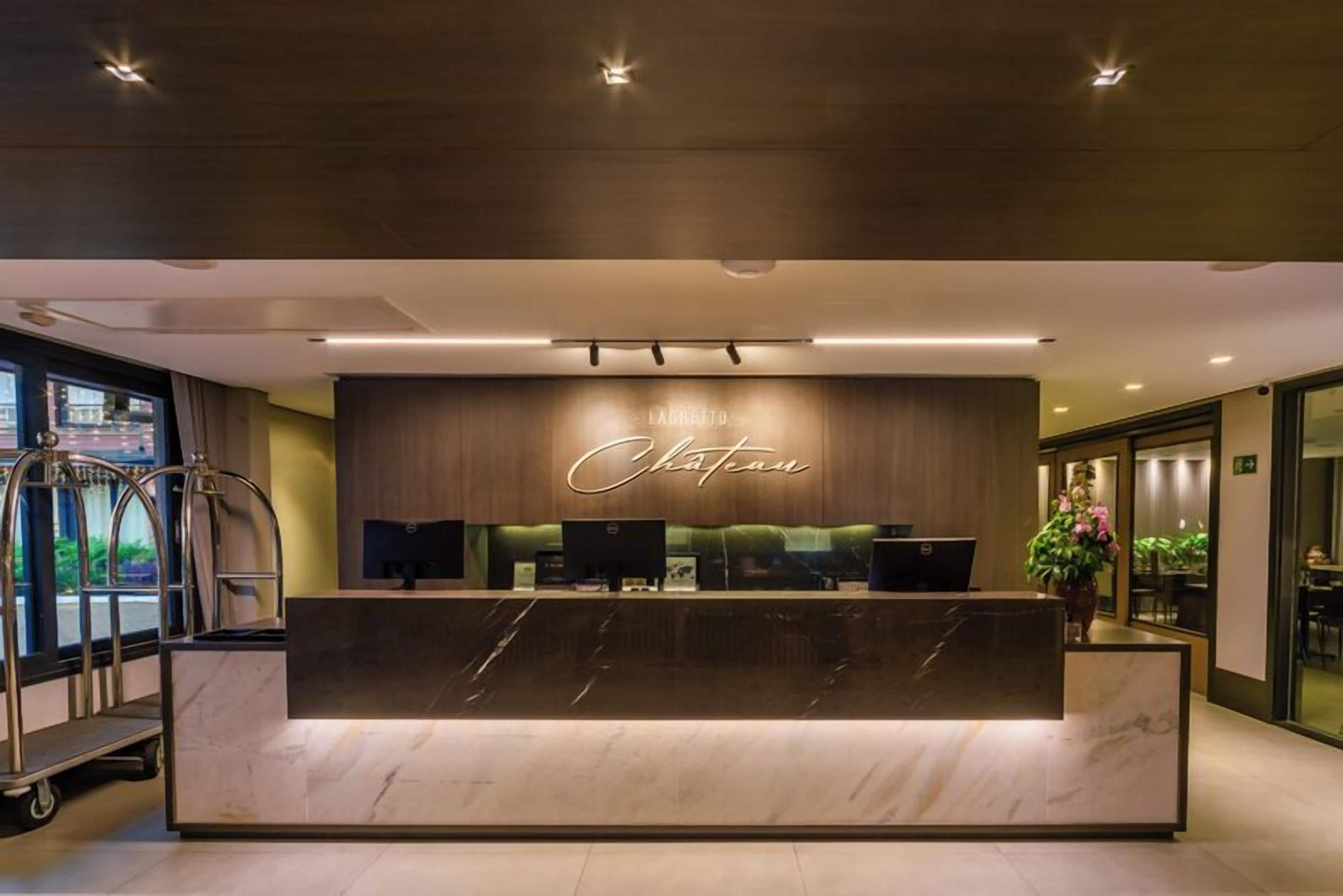 A hotel reception desk with a marble counter, a wooden backdrop with the hotel name, and a reception area with a view of the street outside.