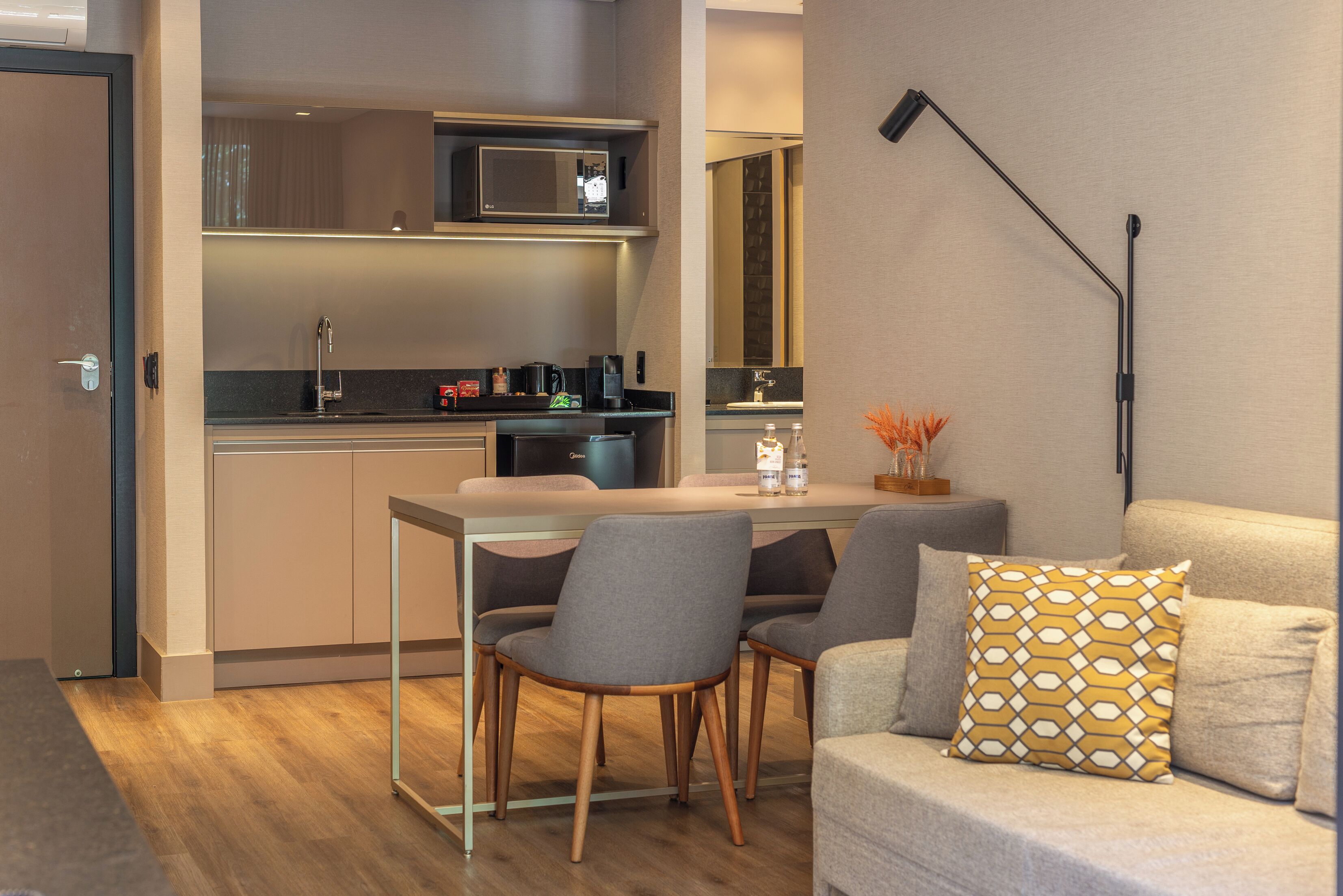 A modern kitchen with a microwave, coffee maker, and a sink. There is a dining area with a table and chairs.