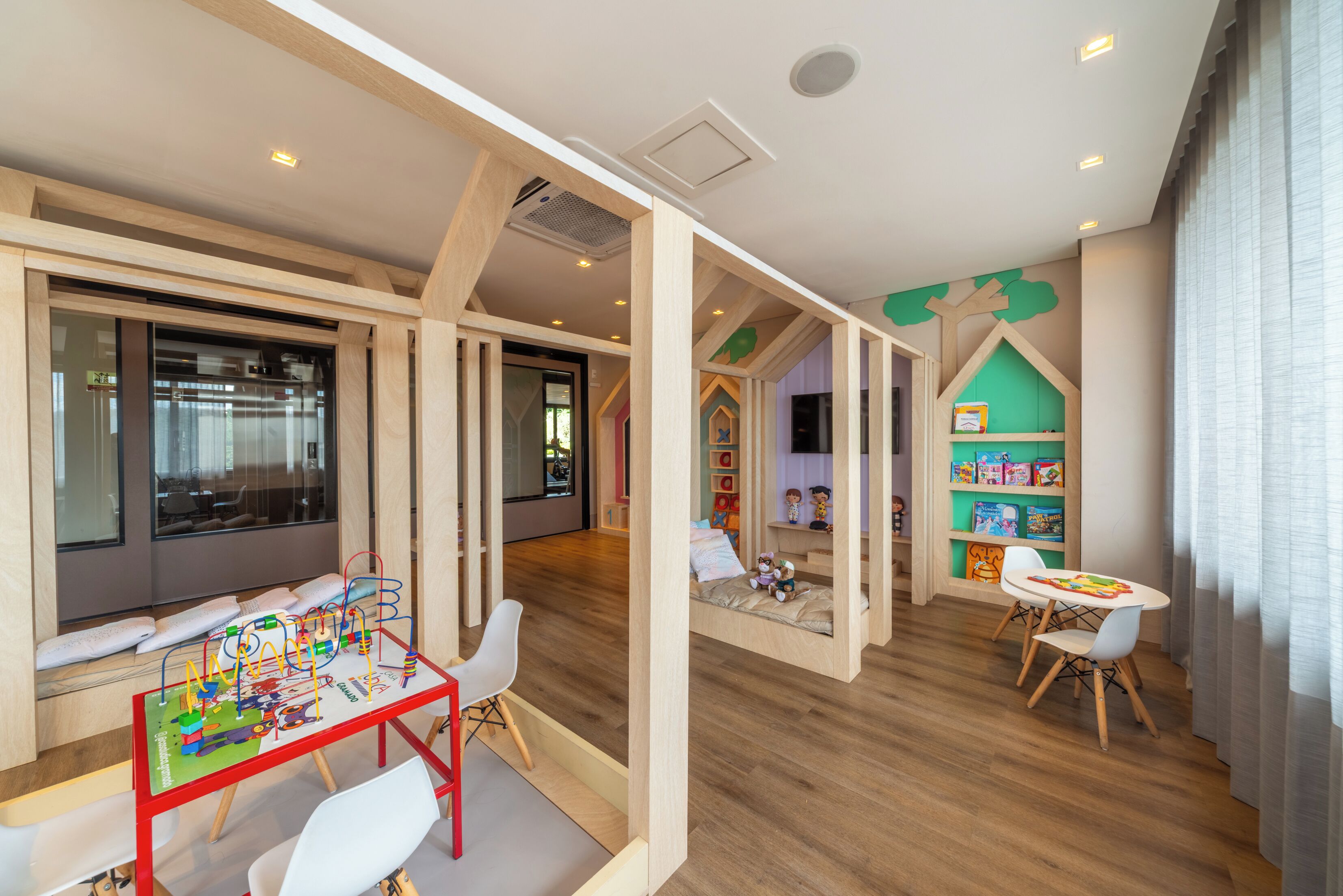 A children's playroom with a wooden play table, white chairs, and a bookshelf.