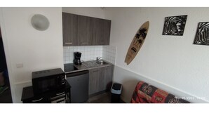 A compact kitchen with grey cabinets, a coffee maker, and a trash bin.