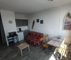 Un espace de vie compact comprenant un coin cuisine, un coin repas avec une table et des chaises, un canapé et un petit banc.