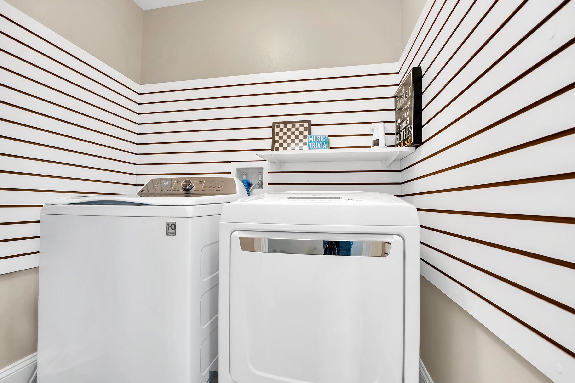 A laundry room with two white washers and dryers, a shelf with a checkered board, and a sign that reads "MUSIC TRIVIA".