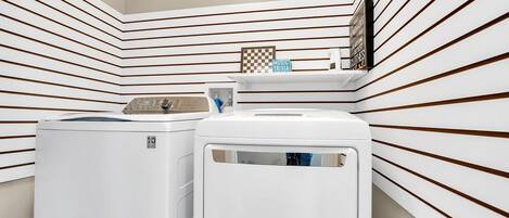 A laundry room with two white washers and dryers, a shelf with a checkered board, and a sign that reads "MUSIC TRIVIA".
