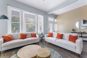 A living room with two white sofas, orange cushions, a round wooden coffee table, and a patterned wall. - *Pearl of Springfield*-WIFI, AC, PATIO (Jacksonville)