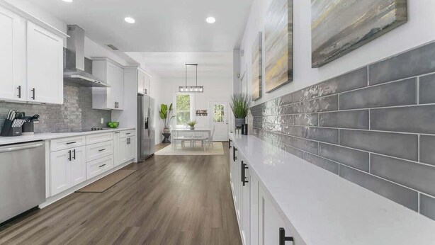 Une cuisine moderne avec des meubles blancs, un dosseret en carrelage gris et un plancher en bois.