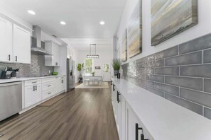 A modern kitchen with white cabinetry, a grey tiled backsplash, and a wooden floor. - Pearl of Springfield -WIFI, AC, PATIO (Jacksonville)