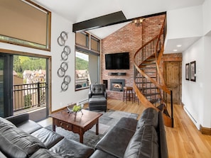 A modern living room with a fireplace, leather sofas, a TV, and a spiral staircase. - Vantage Point Condo 502 (Vail)