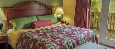 A bedroom with a large bed, two bedside tables with lamps, a bench, and a balcony with a view of greenery.
