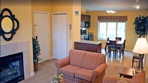 A living room with a fireplace, striped sofa, dining area with chairs, and a kitchen in the background. - 4th of July Week 2024 Massanutten Resort, 2BDRM 2BA Sleeps 6 (Massanutten)