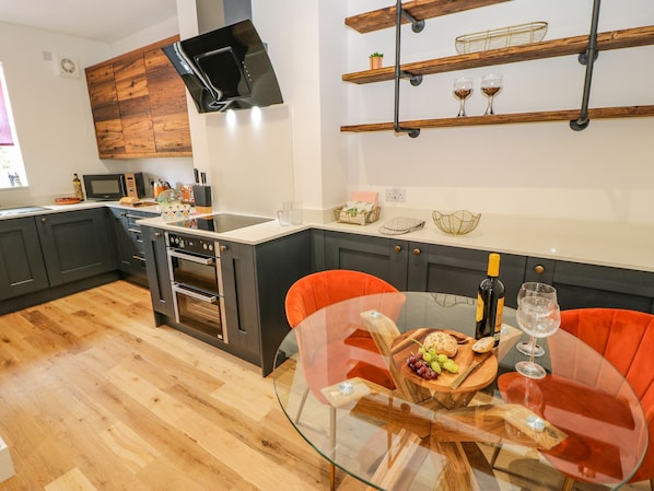 Una cocina moderna con armarios oscuros, microondas, horno y una mesa de comedor de cristal con sillas naranjas.