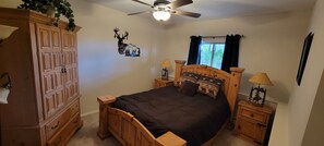 A bedroom with a wooden bed, two bedside tables with lamps, a ceiling fan, a window with curtains, and a wall-mounted deer decoration. - Lush setting, minutes to downtown Colorado Springs (Colorado Springs)