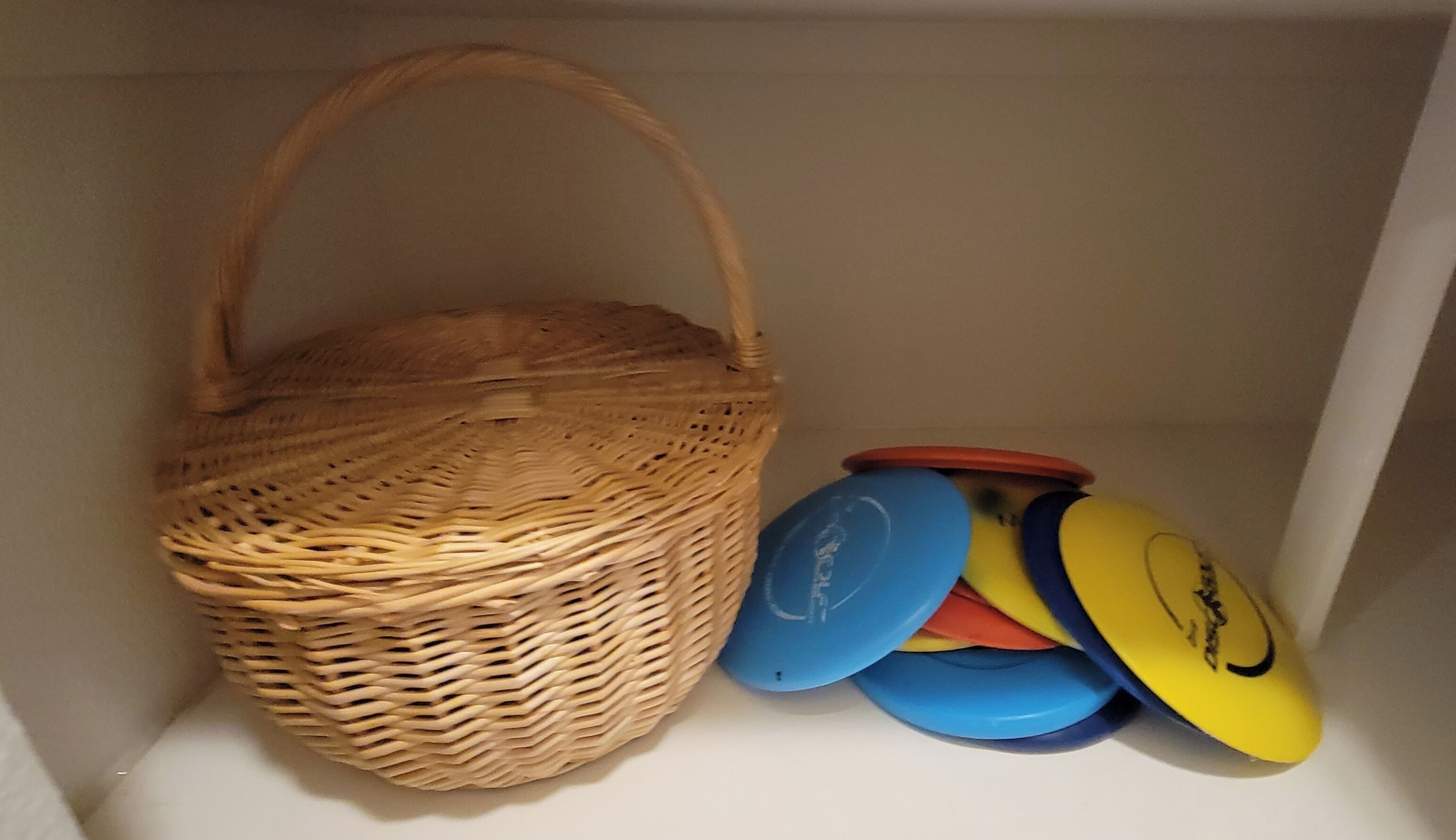 A wicker basket and a stack of colorful frisbees in a white interior space.